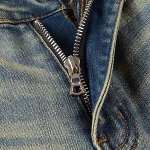 Detail of blue distressed denim jeans with vintage yellow wash and metal zipper fly