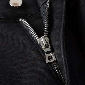 Detailed macro view of black denim fly with silver metal zipper and button closure