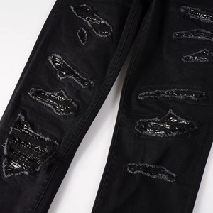 Detail view of black distressed jeans featuring paisley fabric patches inside ripped holes
