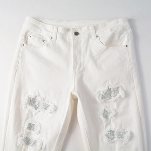 Close-up of white slim fit jeans featuring distressed holes with colorful rhinestones