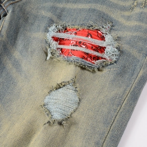 Detail of distressed jeans with ripped holes and red paisley pattern fabric patchwork