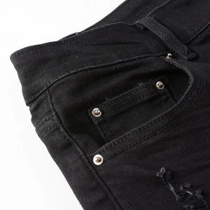 Detail of black street style denim jeans featuring silver metal rivets and distressed rip textures