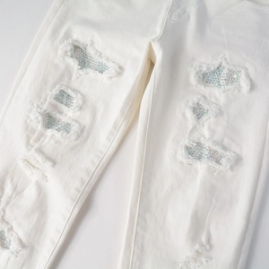 Detail of white ripped denim jeans featuring colorful rhinestone embellishments and frayed edges