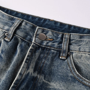 Detail of blue washed denim waist featuring matte silver metal button and rivet reinforcement
