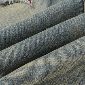 Close-up of distressed blue denim fabric featuring vintage stone wash and worn texture