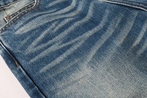 Detail of dark blue denim jeans showing whisker wash effect and orange stitching