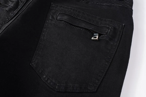 Dettaglio della tasca posteriore in denim nero lavato con zip metallica e pieghe moto