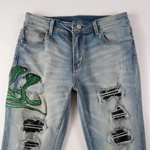 Détail de la broderie serpent vert et des écussons à rayures argentées sur le jean
