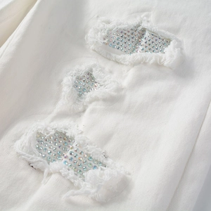 Detail of white denim fabric featuring distressed holes and iridescent rhinestones