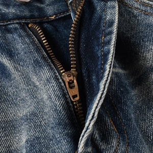 Macro shot of durable bronze YKK zipper and vintage washed denim texture on blue jeans
