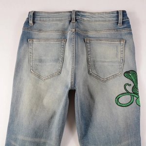 Vue détaillée du jean bleu clair avec broderie cobra verte sur la poche arrière