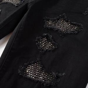Close-up of black denim jeans featuring distressed rips and silver stud embellishments