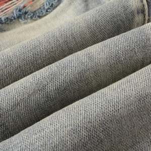 Détail macro du denim bleu clair délavé avec bords usés et coutures rouges contrastées