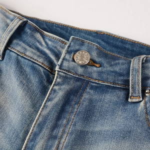 Détail macro de la taille du jean avec bouton en métal, braguette et coutures orange