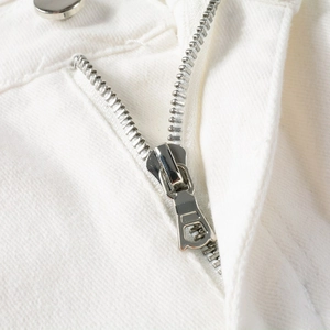 Close-up of high-quality silver metal zipper and white denim fabric texture on jeans