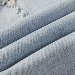 Gros plan du tissu denim bleu clair avec détails déchirés et structure en sergé tissé