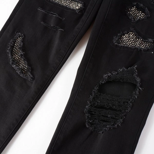 Detail of black distressed denim jeans featuring ripped edges and sparkling silver rhinestones