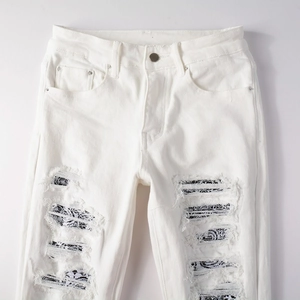 Dettaglio dei jeans bianchi strappati con fodera a motivo paisley nei fori sulle ginocchia