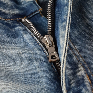 Gros plan sur la braguette zippée et les coutures jaunes du jean bleu délavé