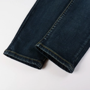 Detailed macro view of deep blue denim jeans cuff showing orange stitching and wash