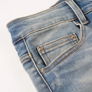 Détail de la poche avant en jean bleu clair avec rivets en cuivre et coutures marron