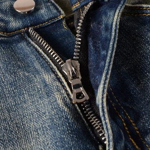 Détail de la fermeture éclair en métal et bouton argenté sur jean bleu avec coutures dorées