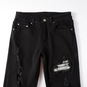 Detailed macro view of distressed black denim with metallic silver patch and ripped accents