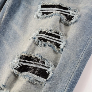 Gros plan d'un jean bleu clair usé avec des empiècements en cuir motif serpent