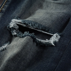 Macro detail of distressed denim jeans with frayed holes and vintage indigo texture