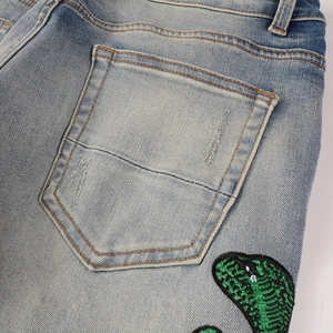 Détail de poche jean déchirée avec broderie cobra vert et texture de délavage usé