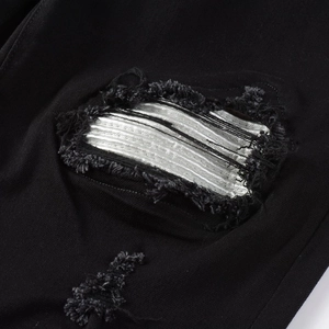Close-up of ripped black denim jeans with metallic silver lining and distressed details