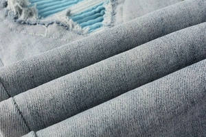 Detail of light blue washed denim with distressed ripped holes and inner fabric patches