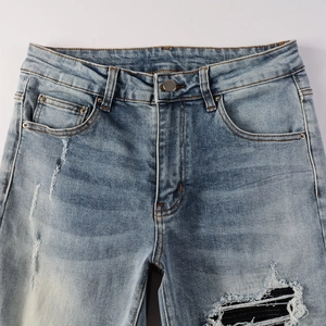 Detailed close-up of light blue distressed jeans with black patchwork and metal rivets