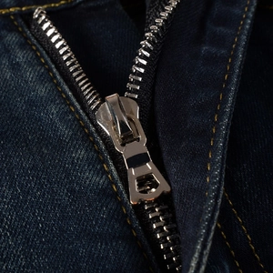 Detailed close-up of heavy-duty metal zipper and double stitching on dark blue denim pants