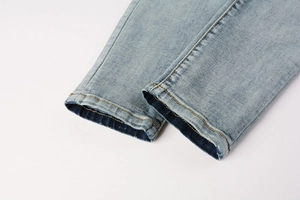 Detailed close-up of distressed denim hem with yellow double stitching on blue jeans
