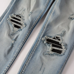 Detail of light blue distressed jeans featuring biker-style ribbed patches on knee rips