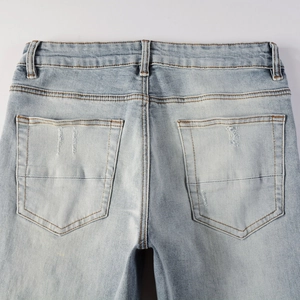 Detail of light blue washed denim jeans featuring distressed pockets and contrast stitching