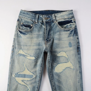 Detail of light blue distressed jeans showing ripped knee with reinforced fabric patch