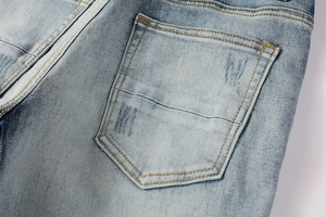 Detail of light blue denim jeans showing the back pocket with W-shaped distressing and heavy wash