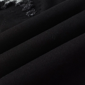 Close-up of black denim fabric texture with distressed ripped edge and diagonal twill detail