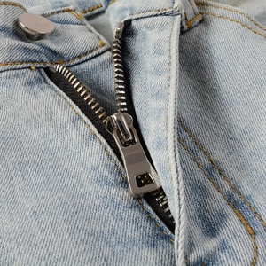 Close-up of metal zipper fly and silver button on light blue denim biker jeans