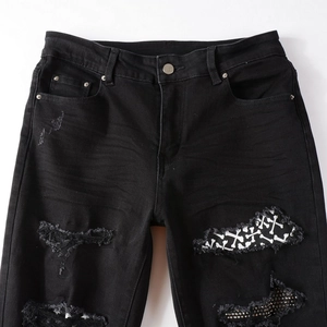 Detail of distressed black denim jeans with ripped holes and white bone pattern patches