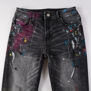 Detailed view of black slim-fit distressed jeans with vibrant colorful paint splatter