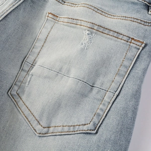 Detail of light blue denim back pocket featuring distressed holes and orange stitching