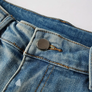 Macro shot of silver metal button and yellow contrast stitching on washed blue denim jeans