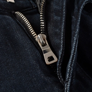 Macro shot of silver metal zipper closure on deep navy slim fit denim biker jeans