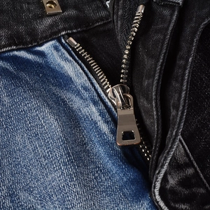 Detail of silver metal zipper and dual-tone patchwork denim fabric on biker jeans
