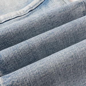 Gros plan sur la texture du denim bleu clair et les coutures blanches du jean de moto