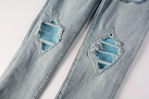 Detailed close-up of light blue washed denim with corduroy patches and distressed knees