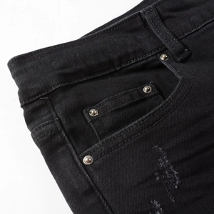 Detail of black slim-fit jeans showing denim texture, rivets, and distressed ripped holes